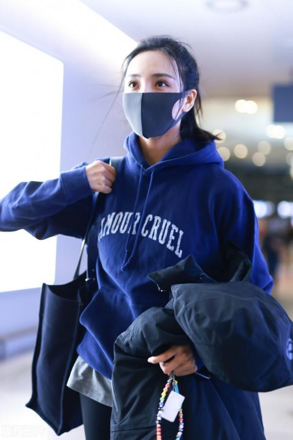 王紫璇穿藍色字母衛衣搭配小黑褲，手拿短款羽絨服溫暖陽光