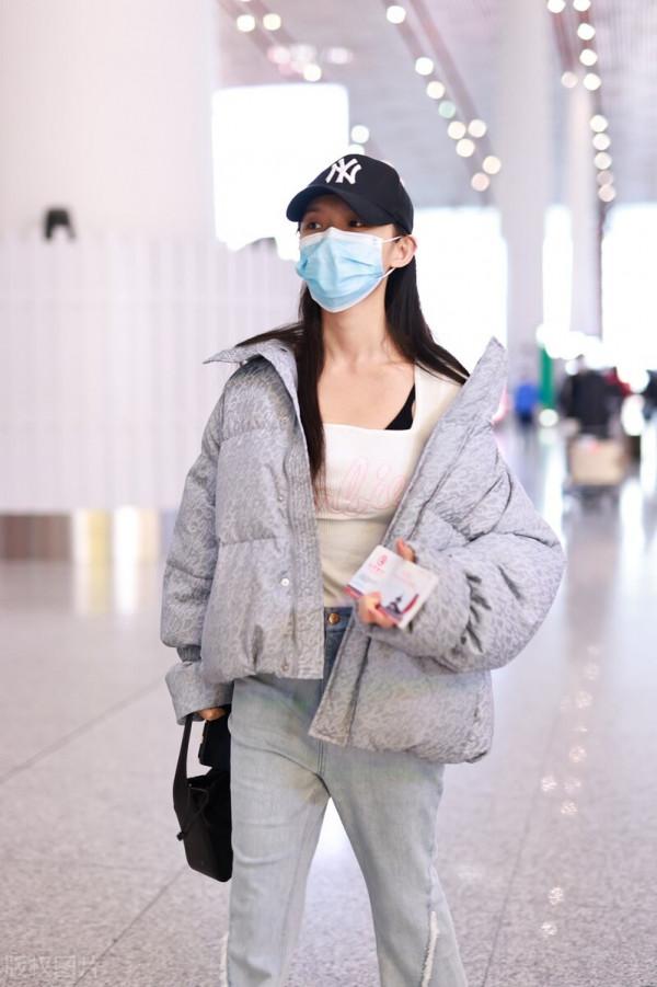 林允穿灰色羽絨服搭配牛仔開衩褲，戴棒球帽溫暖時尚