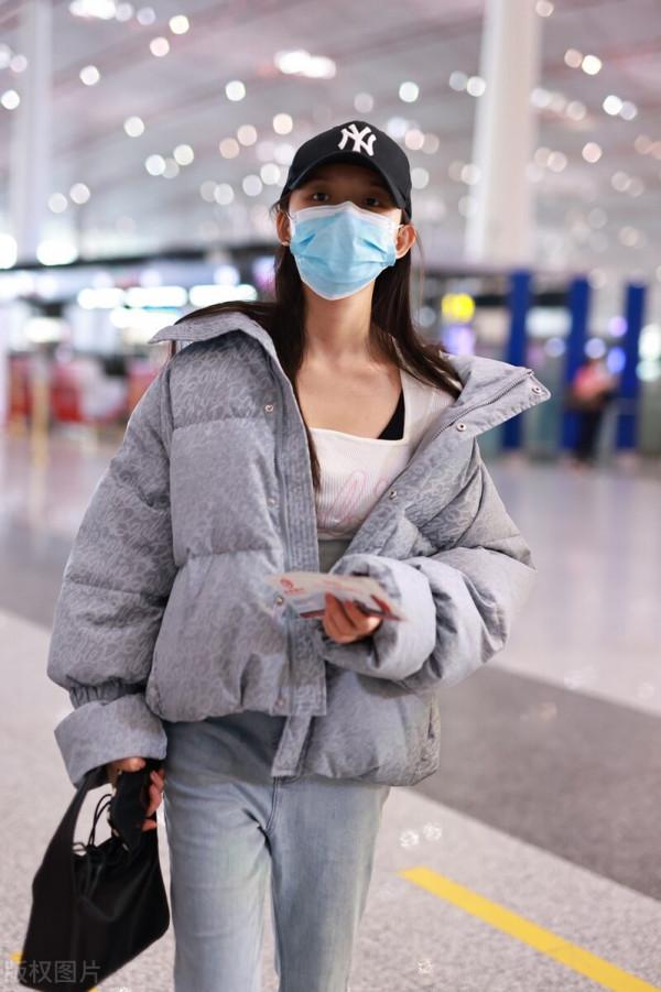 林允穿灰色羽絨服搭配牛仔開衩褲，戴棒球帽溫暖時尚